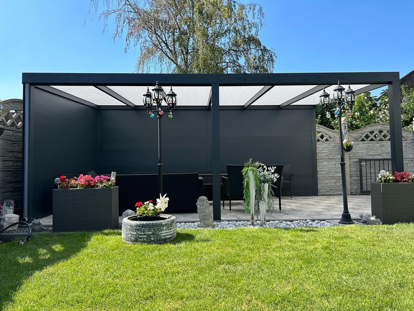 Frontale Ansicht der Terrassenüberdachung mit Blumen und Trauerweide